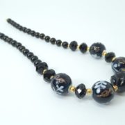 Gros plan sur les perles du collier noir et or.