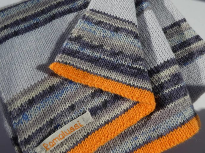 L'étiquette Pamalussi et les rangs en laine orange au bord de l'écharpe en laine à rayures bleues.