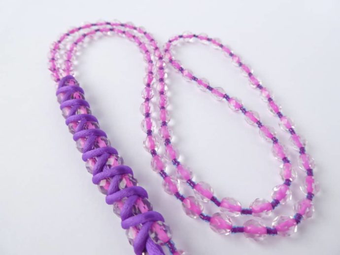Les deux extrémités du long collier rose et violet reliées par un cordon.