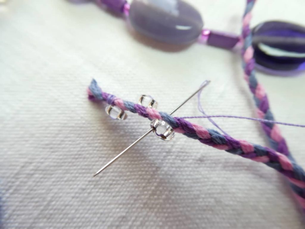 Perles translucides cousues sur le cordon violet du collier Valentine.