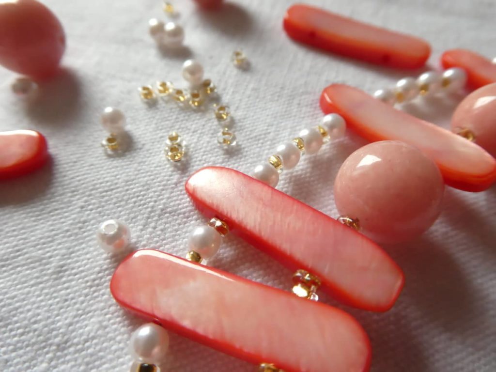 Gros plan sur l'enfilage des perles spacer Miyuki du collier 2 rangs rose saumon.