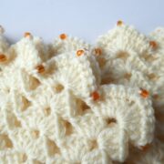 Détail des coquilles et des perles oranges des manchettes crème.
