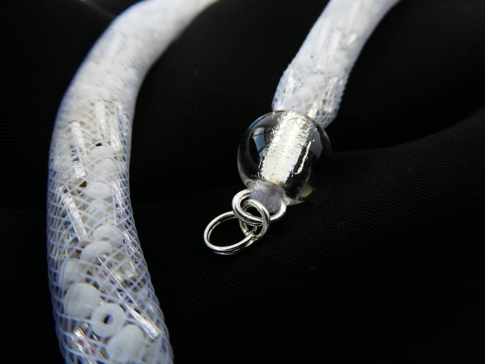 La résille tubulaire du collier blanc Filipa garnie de perles de rocailles et de mini tubes cristal argent.